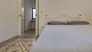 Un dormitorio con una cama, un tapete estampado y una puerta que da a otra habitación.