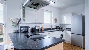 A modern kitchen with a granite countertop, stainless steel appliances, and white cabinetry. - Skyline Duplex Penthouse - Llanelli (Llanelli)