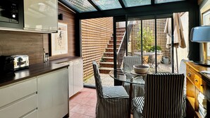 Une cuisine moderne équipée d’un four à micro-ondes encastré, d’un grille-pain et d’un meuble en bois. Une porte en verre donne sur un patio extérieur agrémenté d’une table, de chaises et d’un mur en briques.