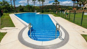 Una piscina rectangular amb vora corbada, envoltada per una tanca verda i palmeres.