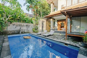 A swimming pool with lounge chairs, surrounded by tropical plants and a covered patio area. - Sebudjan Grand Aurora (Ubud)