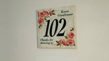 Señal para la Habitación Gianfranco, número 102, con un diseño floral y la silueta de una persona.
