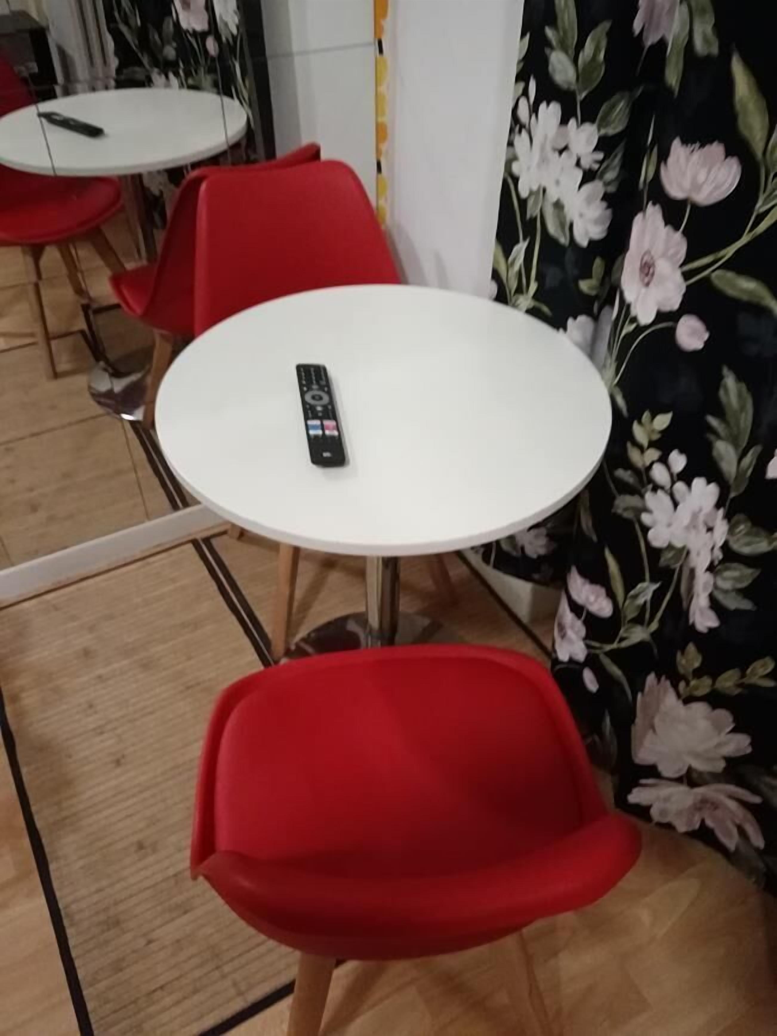 Un espace repas avec des tables rondes blanches et des chaises rouges. Une télécommande est posée sur l’une des tables.