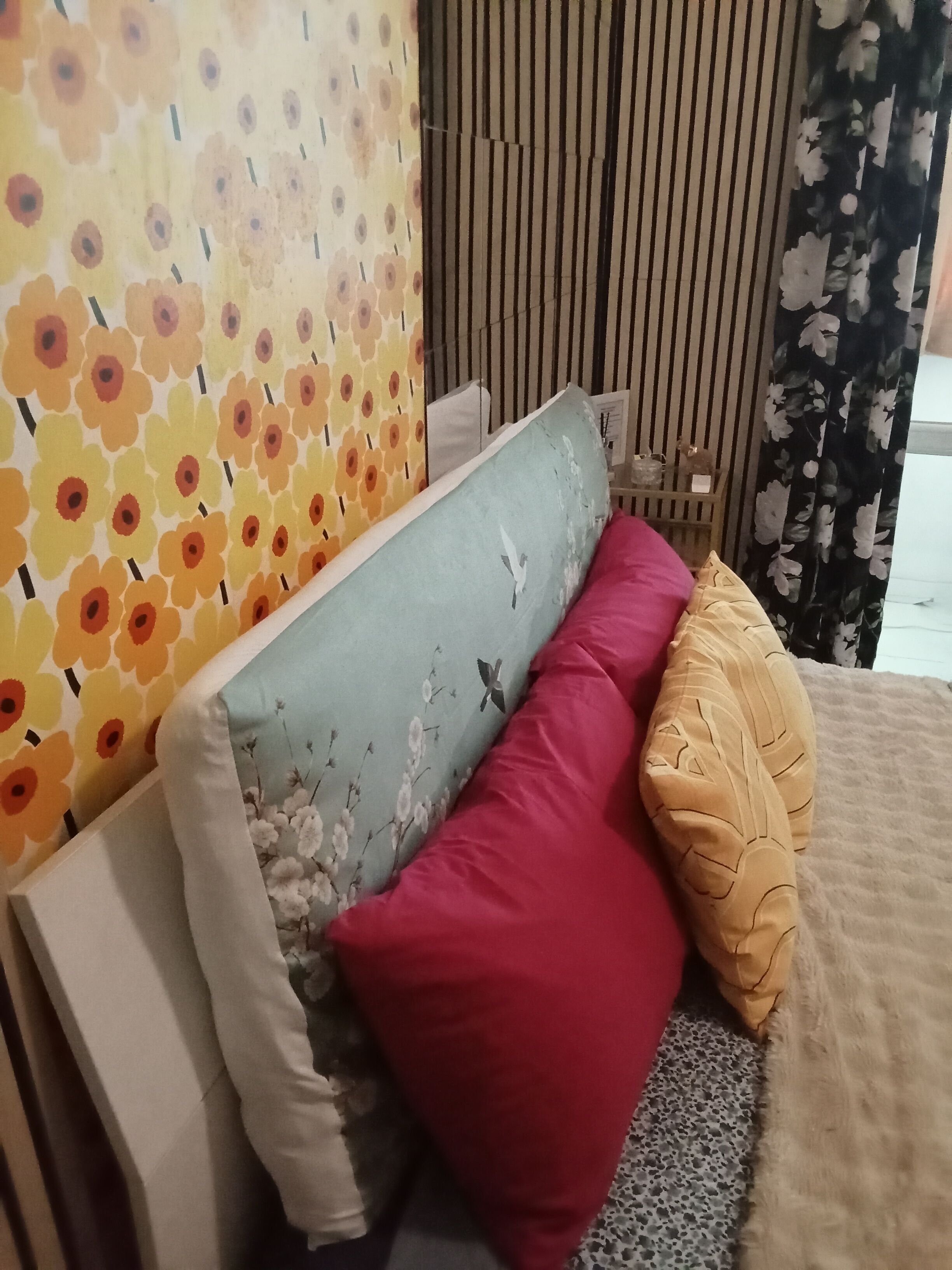 Un letto con una testiera a motivi floreali, un cuscino grigio, un cuscino rosso e un cuscino giallo.