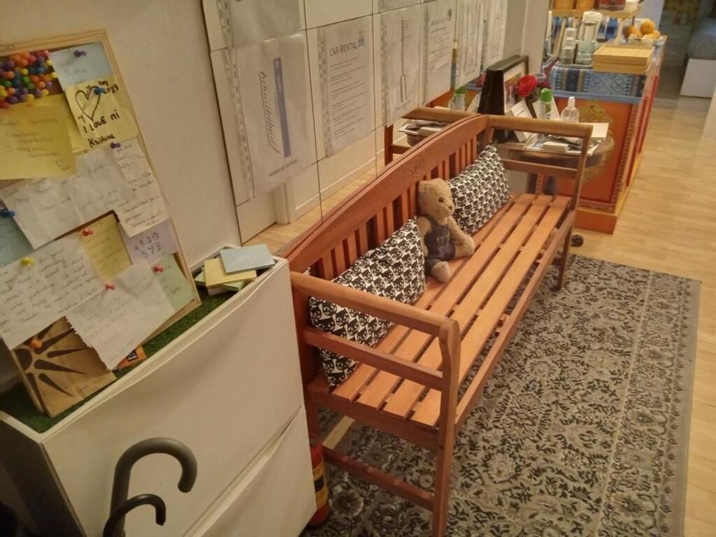 Eine hölzerne Bank mit einem Teddybären, einem gemusterten Kissen und einem kleinen Tisch mit einem Blumenstrauß.