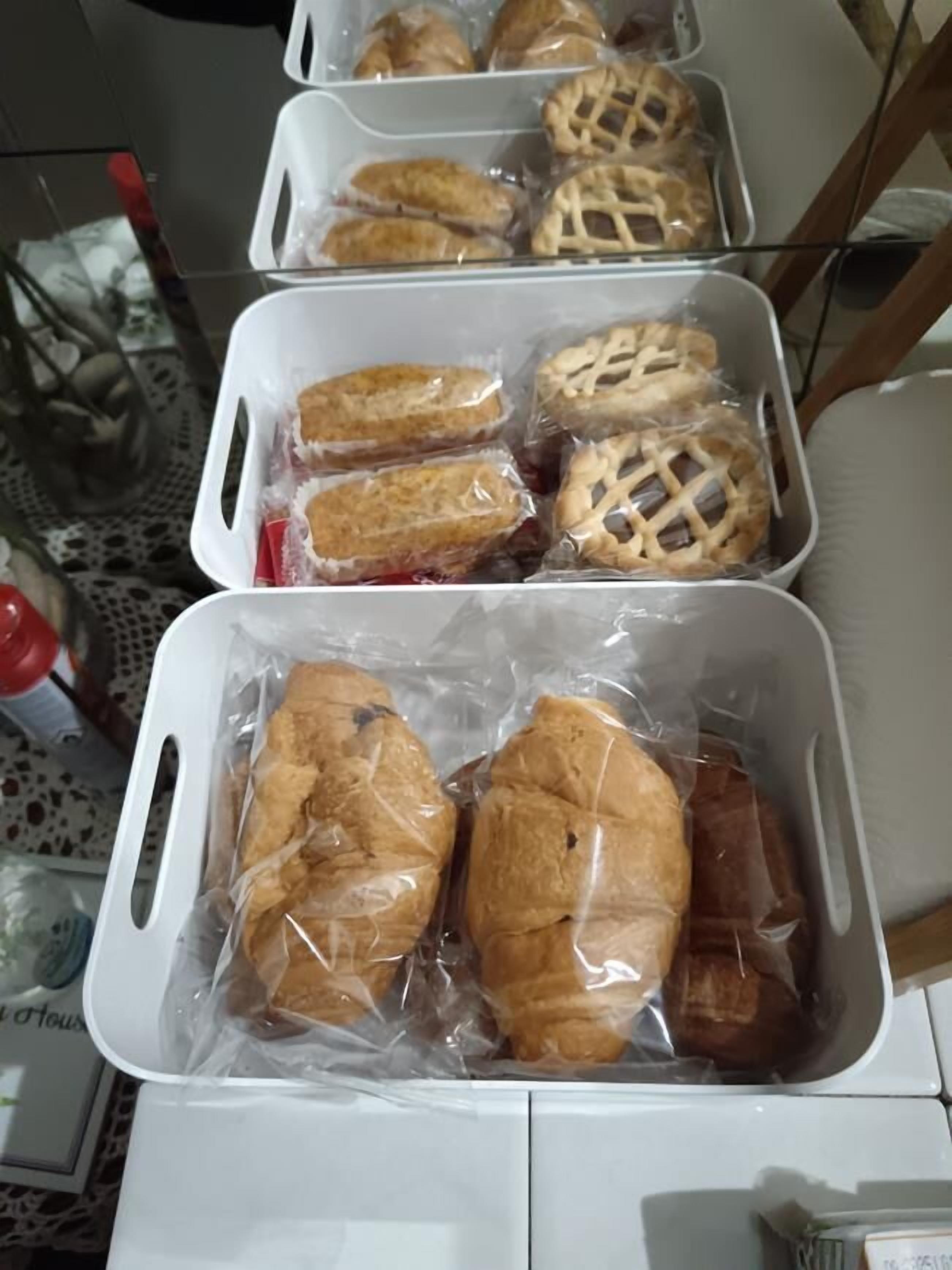 Trois récipients en plastique contenant divers produits de boulangerie, notamment des tartes et des pâtisseries, sont posés sur une table.