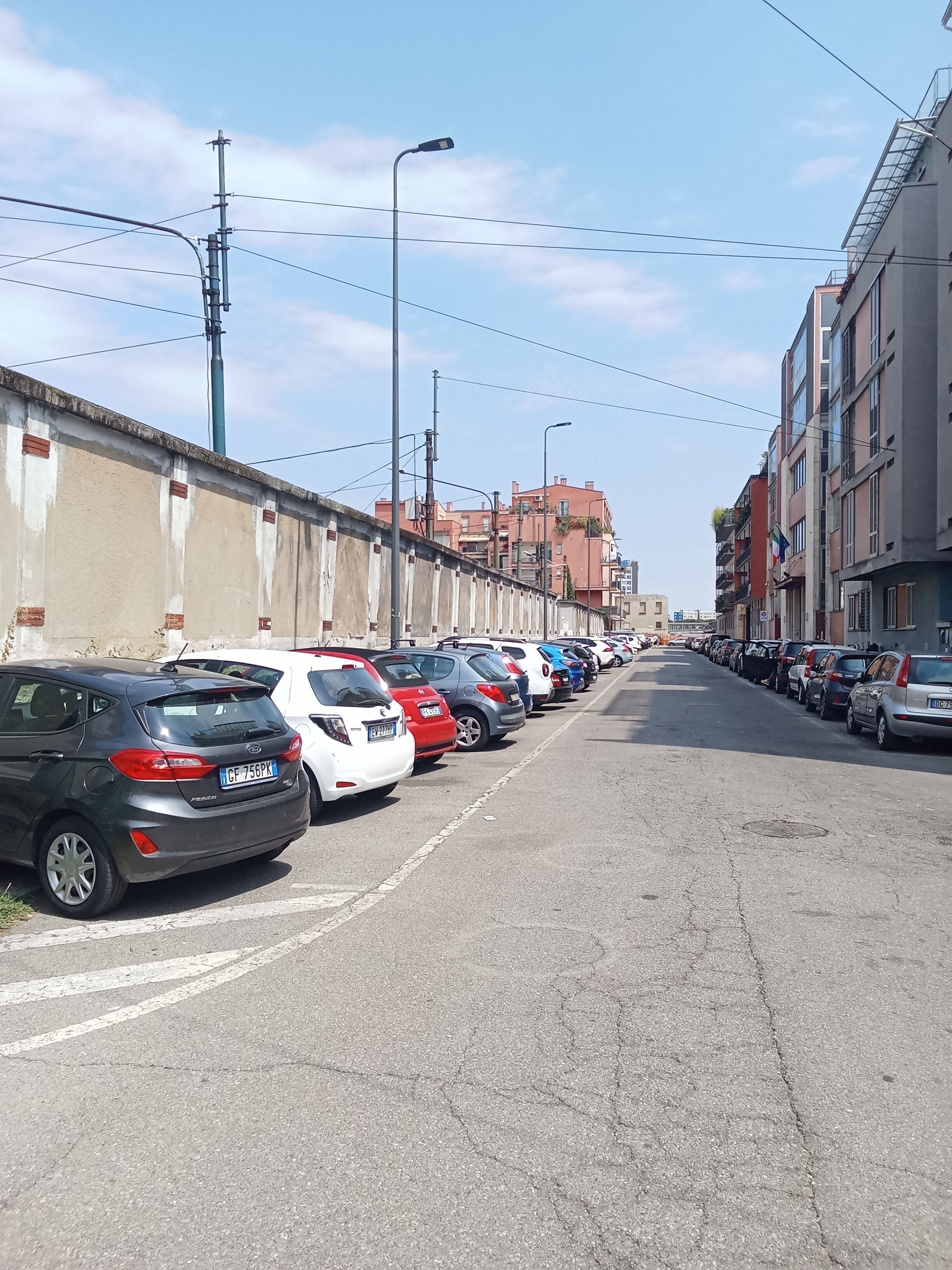 Une rangée de voitures garées le long d’une rue, avec des immeubles d’un seul côté.