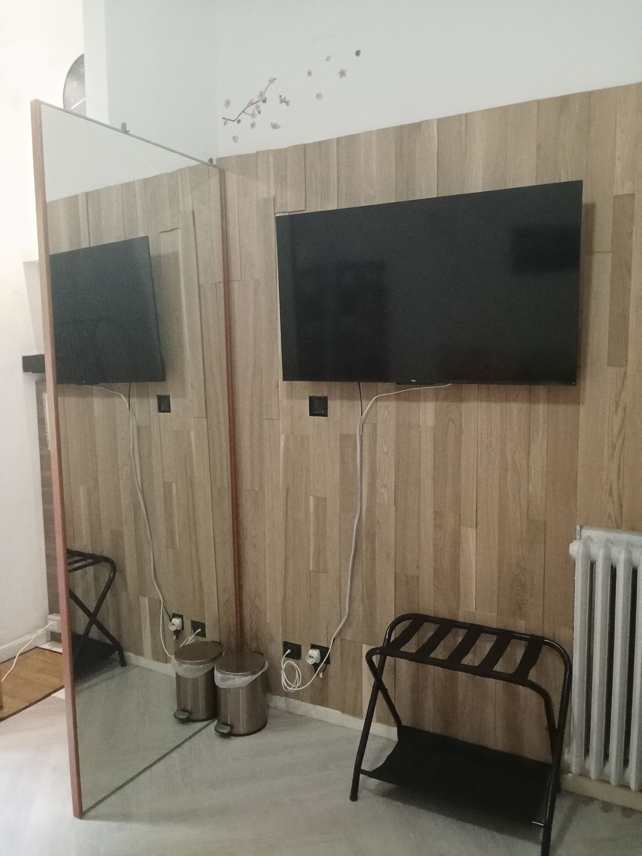 A room with a mirrored partition, a black bench, a radiator, and a wall-mounted television.