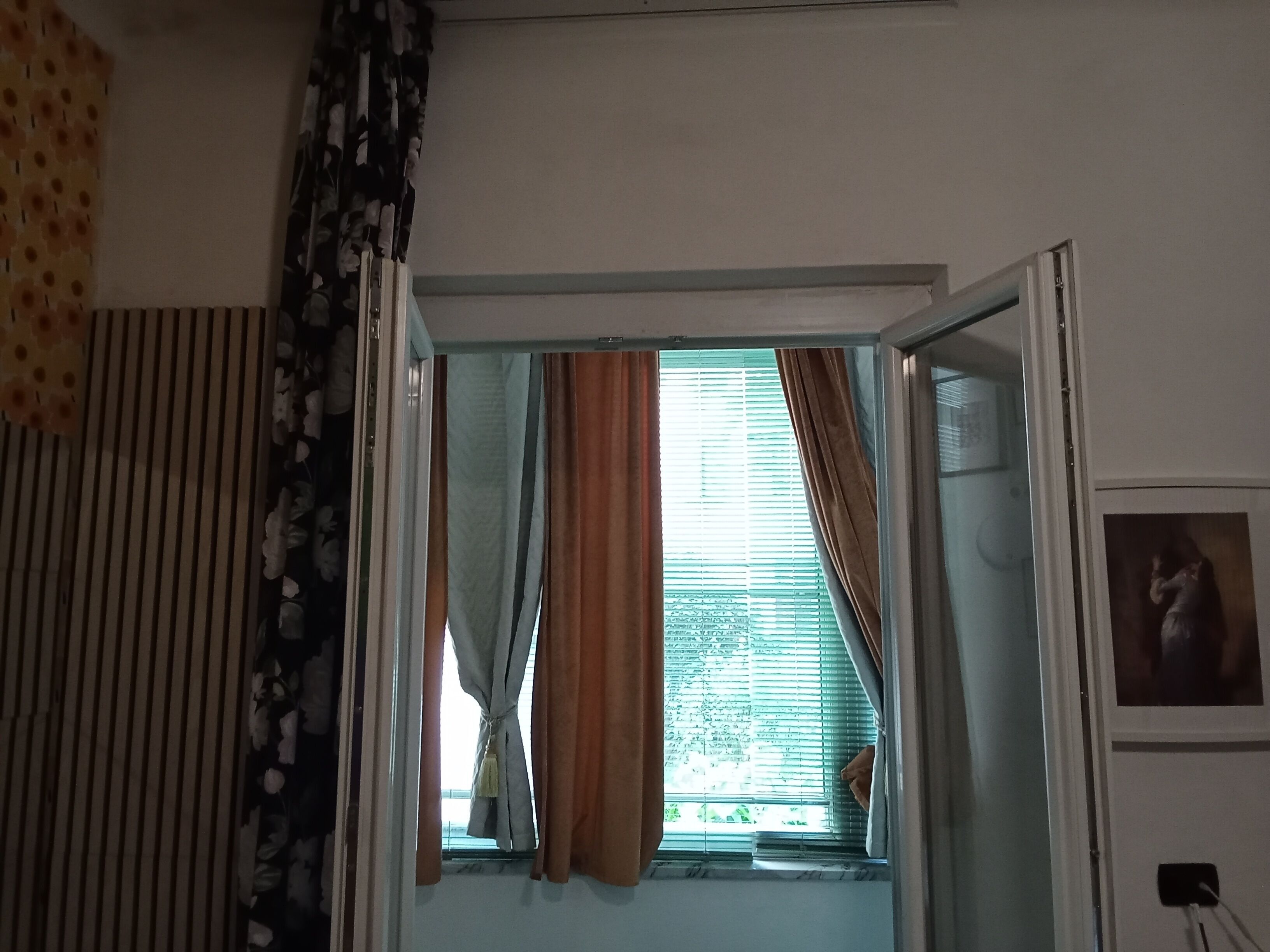 An open doorway leading to a room with a window, curtains, and a partial view of a wall with a picture frame.