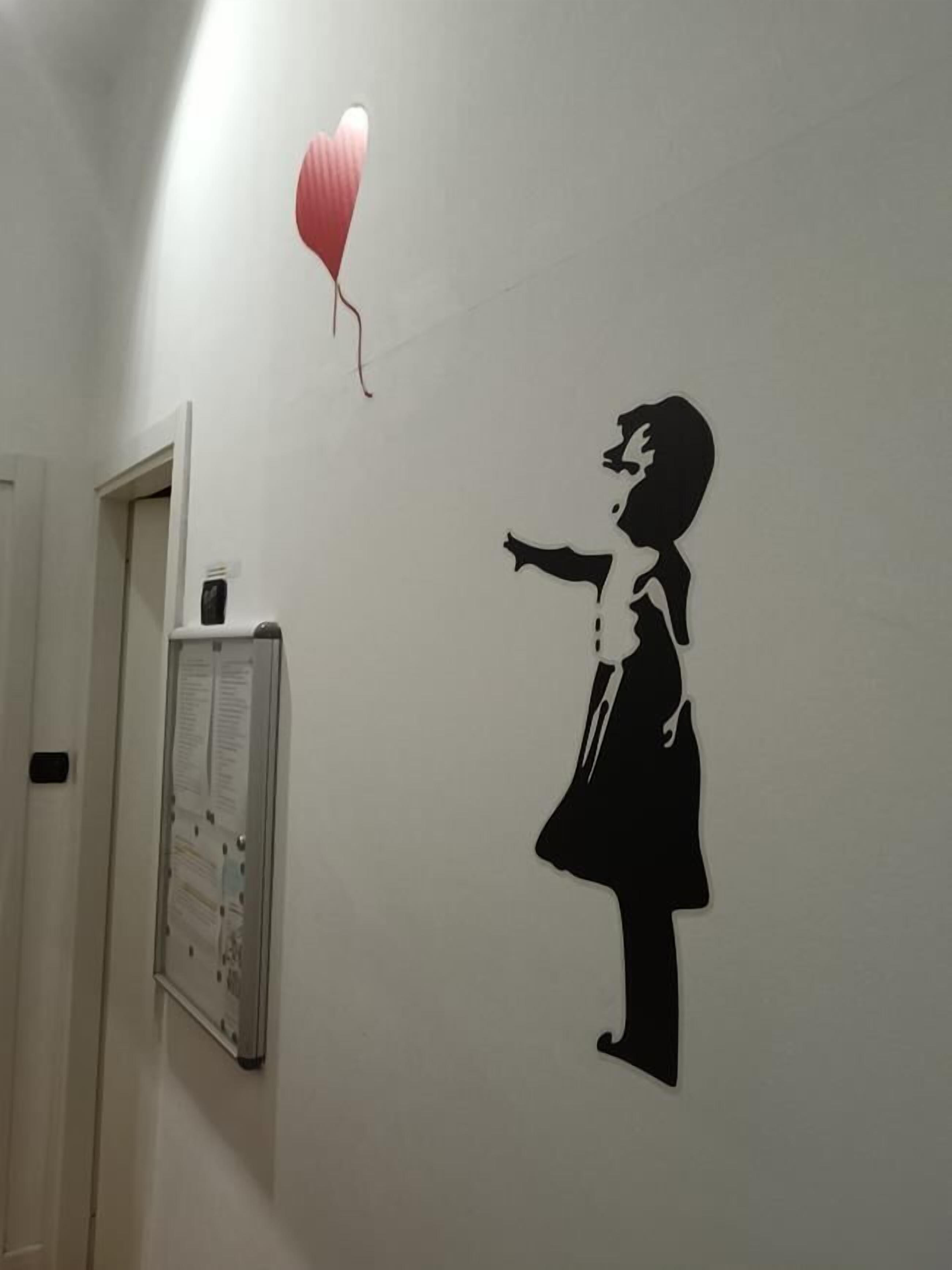 A wall with a black silhouette of a child reaching for a red heart-shaped balloon.