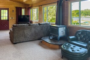 A cozy living room with a sectional sofa, a fireplace, and large windows offering a view of the outdoors. - 'Wet Feet Retreat' Year-Round Cabin in Frederic (Frederic)