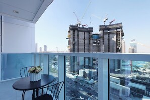 A balcony with a table and chairs, overlooking a cityscape with construction cranes and high-rise buildings.