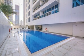 A swimming pool adjacent to a modern building with multiple floors and balconies.