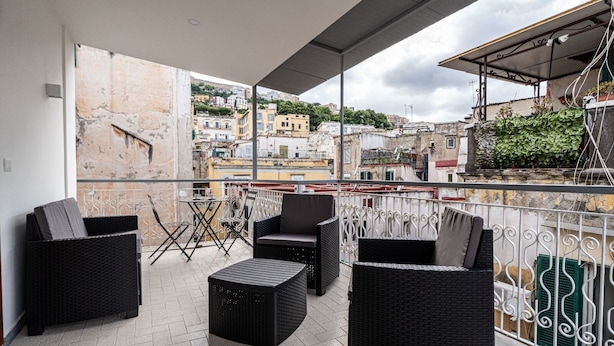 A balcony with wicker furniture, a small table, and a view of the cityscape. - La Maison di Tina (Naples)