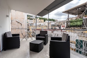 Uma varanda com móveis de vime, uma mesa pequena e vista para a cidade.