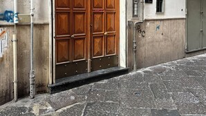 A large wooden door with a metal handle, a small window with a sign, and a number '56' on the wall. - La Maison di Tina (Naples)