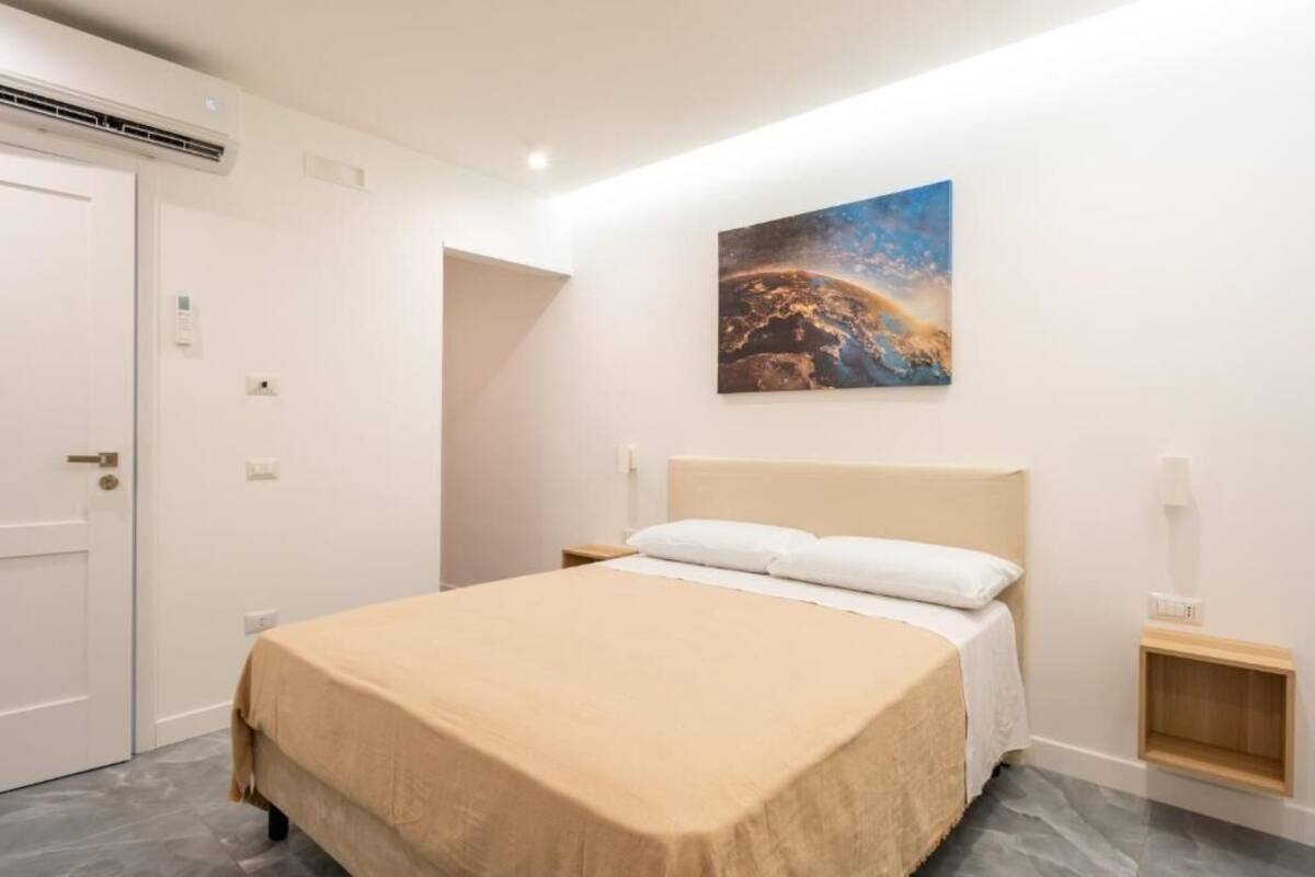 A bedroom with a bed, a nightstand, a wall-mounted painting, and a door.