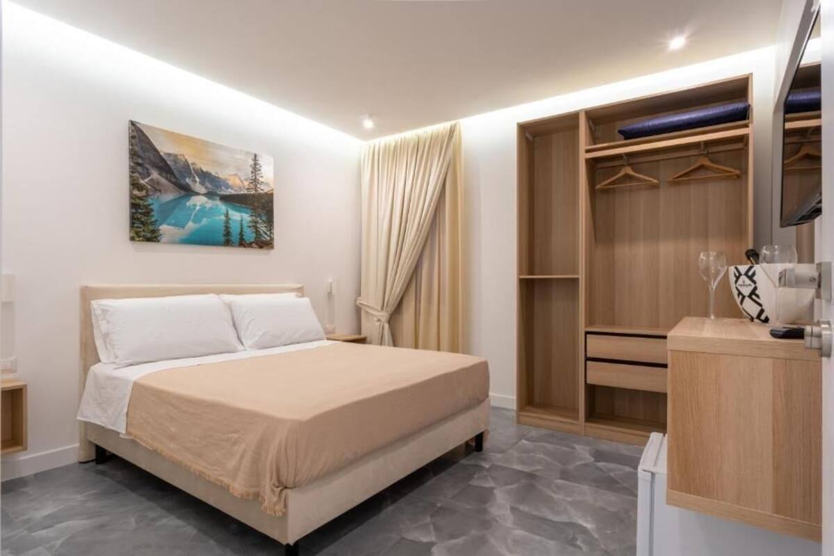 A modern bedroom with a bed, a wardrobe, a desk, and a painting on the wall.