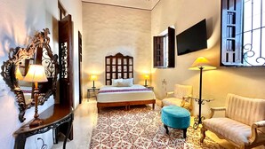 A bedroom with a bed, a chair, a table, a mirror, and a TV. - Majestic Colonial Modern House@Santiago BELLE RIVE (Mérida)
