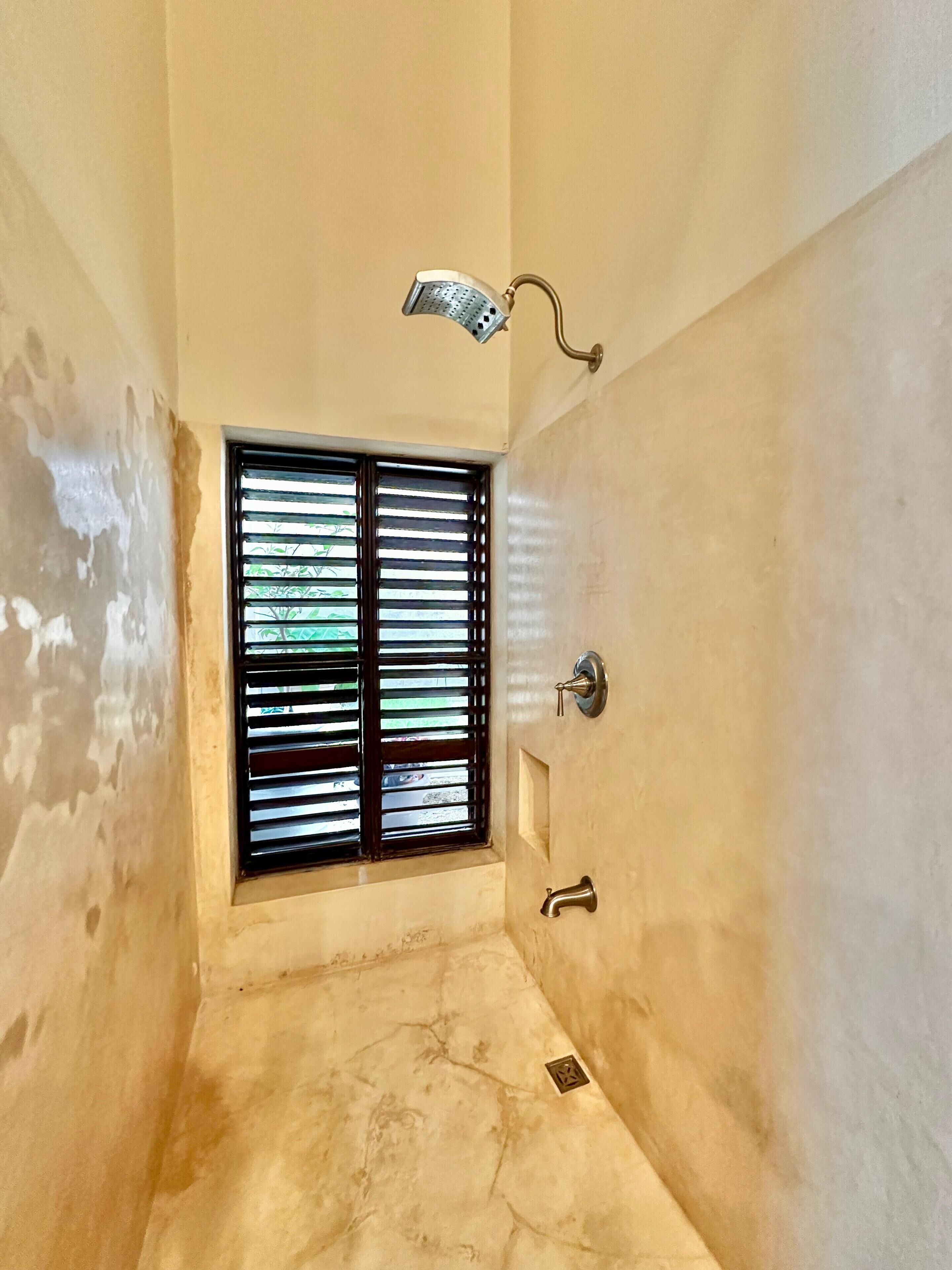 A narrow, unfinished bathroom with a window and a shower.