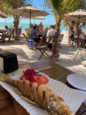 A beachside dining area with tables, umbrellas, and a large fish dish on a table. - Majestic Colonial Modern House@Santiago BELLE RIVE (Mérida)