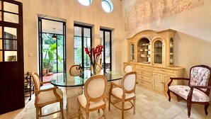 A dining area with a glass table surrounded by wooden chairs, a cabinet with glass doors, and a view of greenery outside. - Majestic Colonial Modern House@Santiago BELLE RIVE (Mérida)