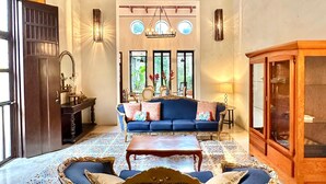 A spacious room with a high ceiling, a blue sofa set, a wooden cabinet, and patterned floor tiles. - Majestic Colonial Modern House@Santiago BELLE RIVE (Mérida)