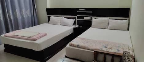 A hotel room with two single beds, a small table, and a chair.