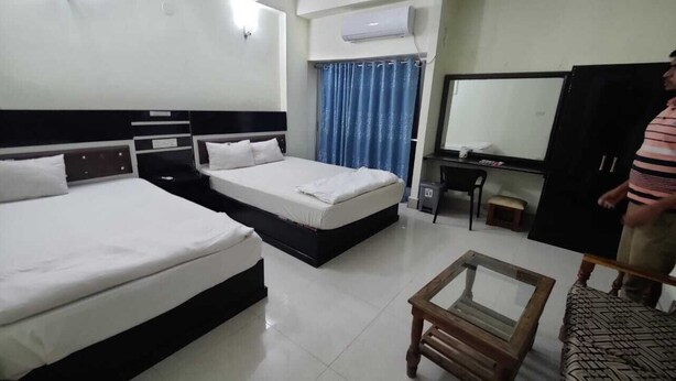 A hotel room with two beds, a desk, a chair, and a wardrobe. - Hotel Aman International (Kalapara)