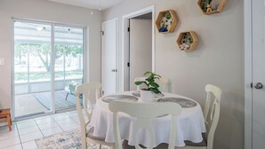 Un coin repas avec une table ronde, des chaises blanches et une plante en pot. Trois décorations hexagonales en bois ornent le mur.
