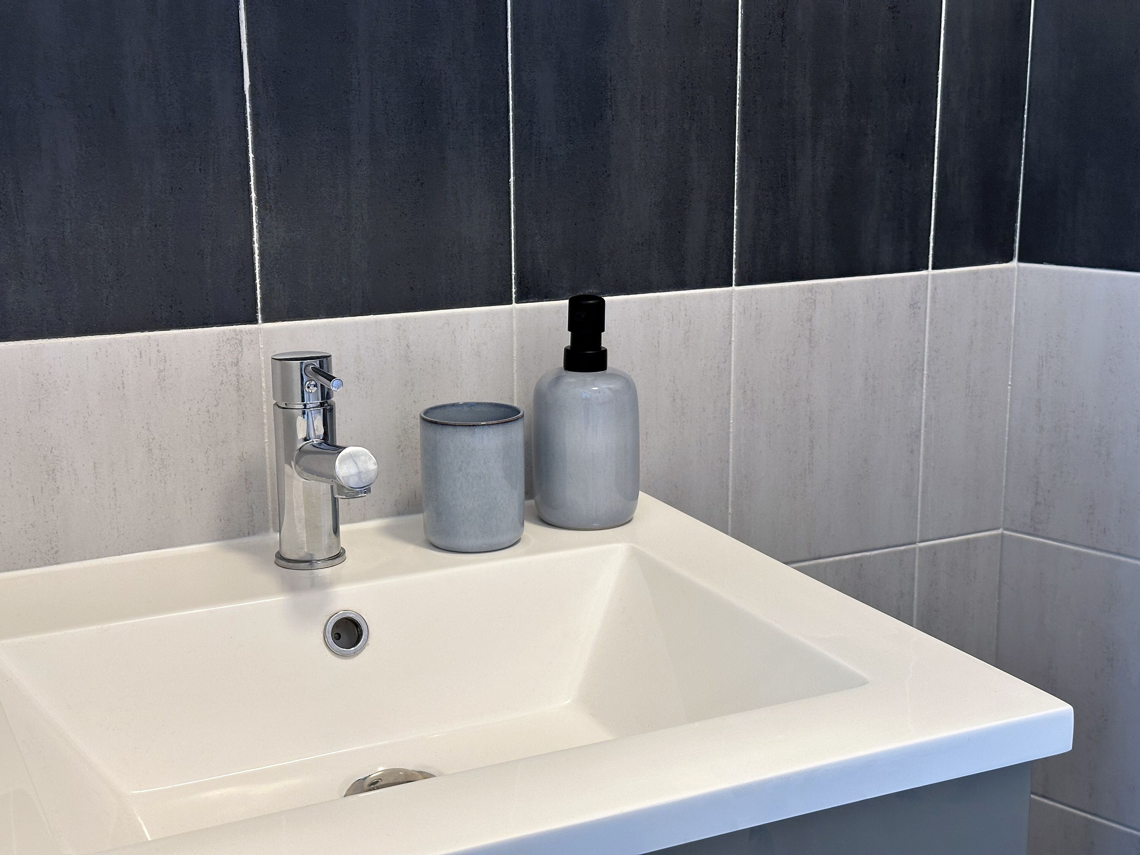 A bathroom sink with a modern faucet, a soap dispenser, and a cylindrical container.