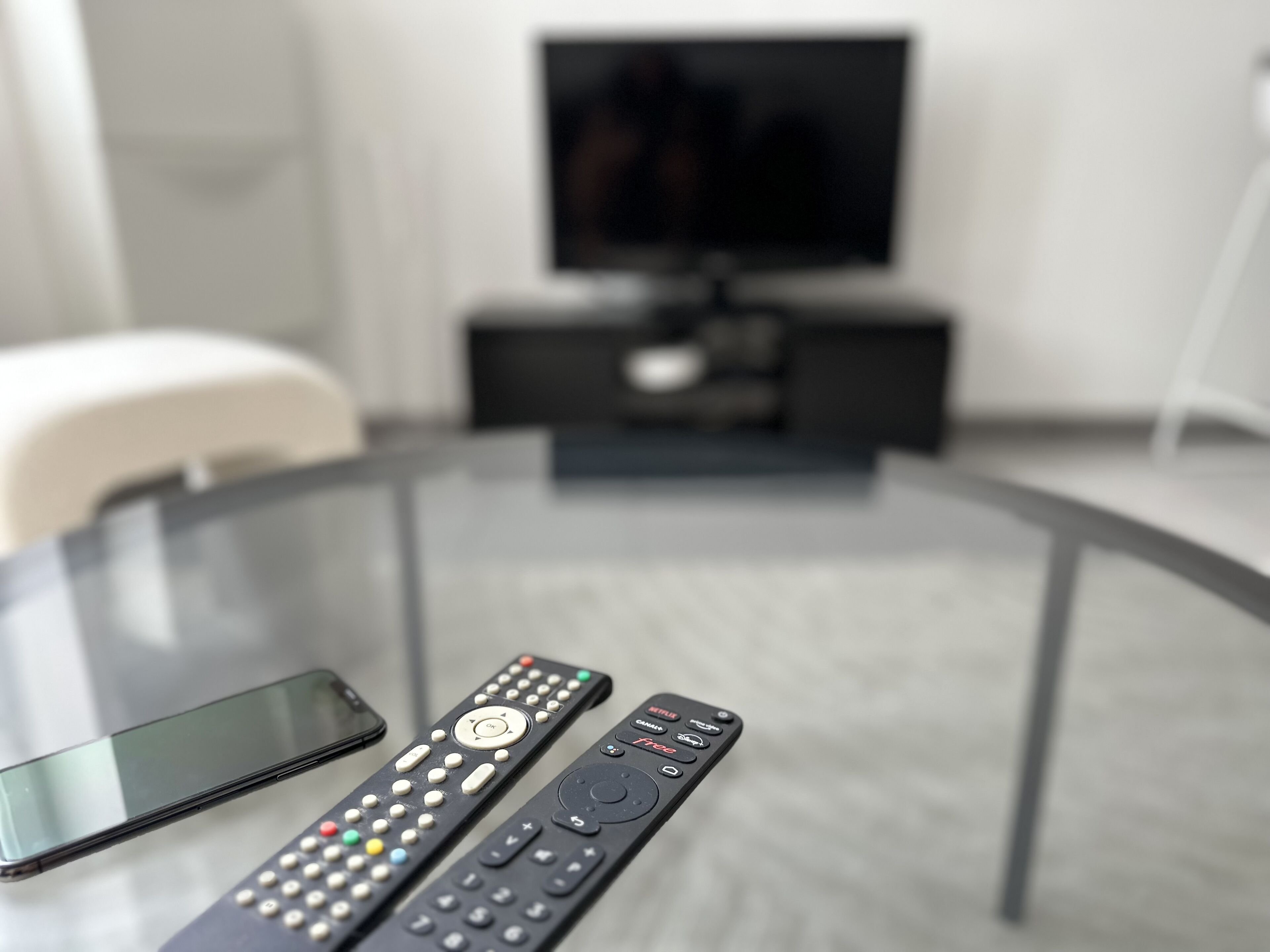 Une table en verre sur laquelle reposent deux télécommandes et un téléphone intelligent.