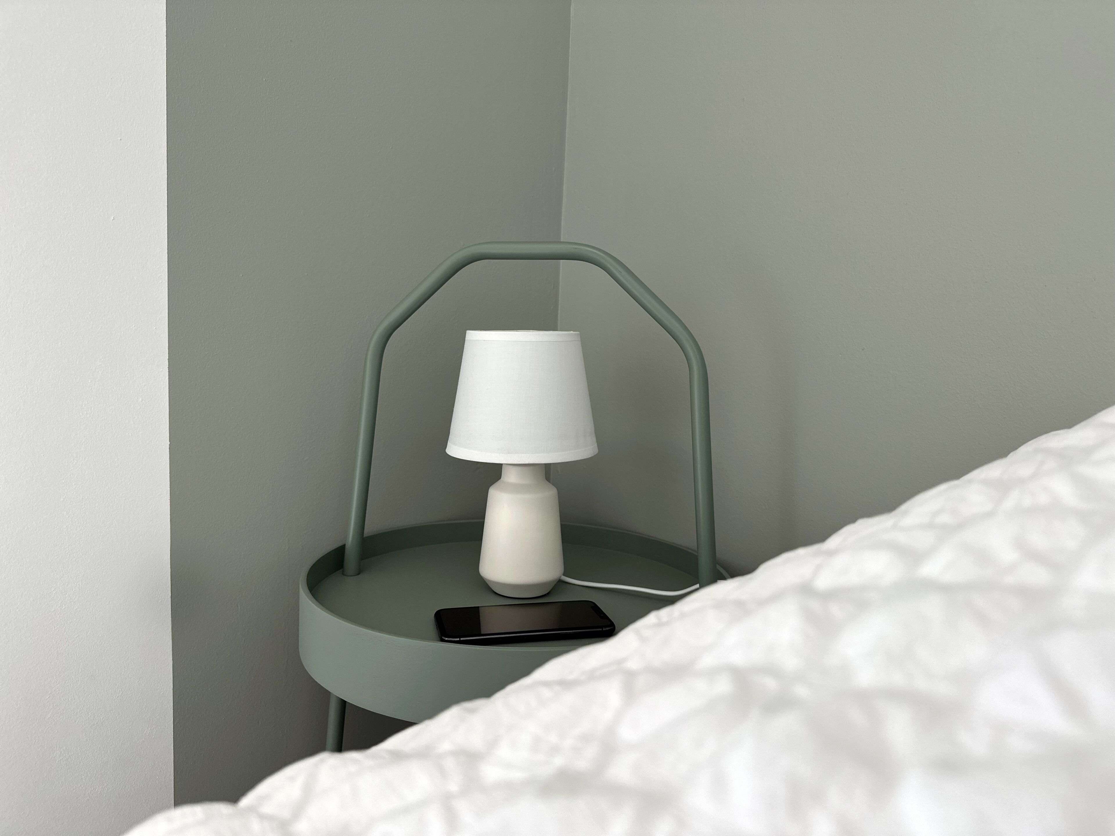 A bedside table with a lamp and a smartphone on it.