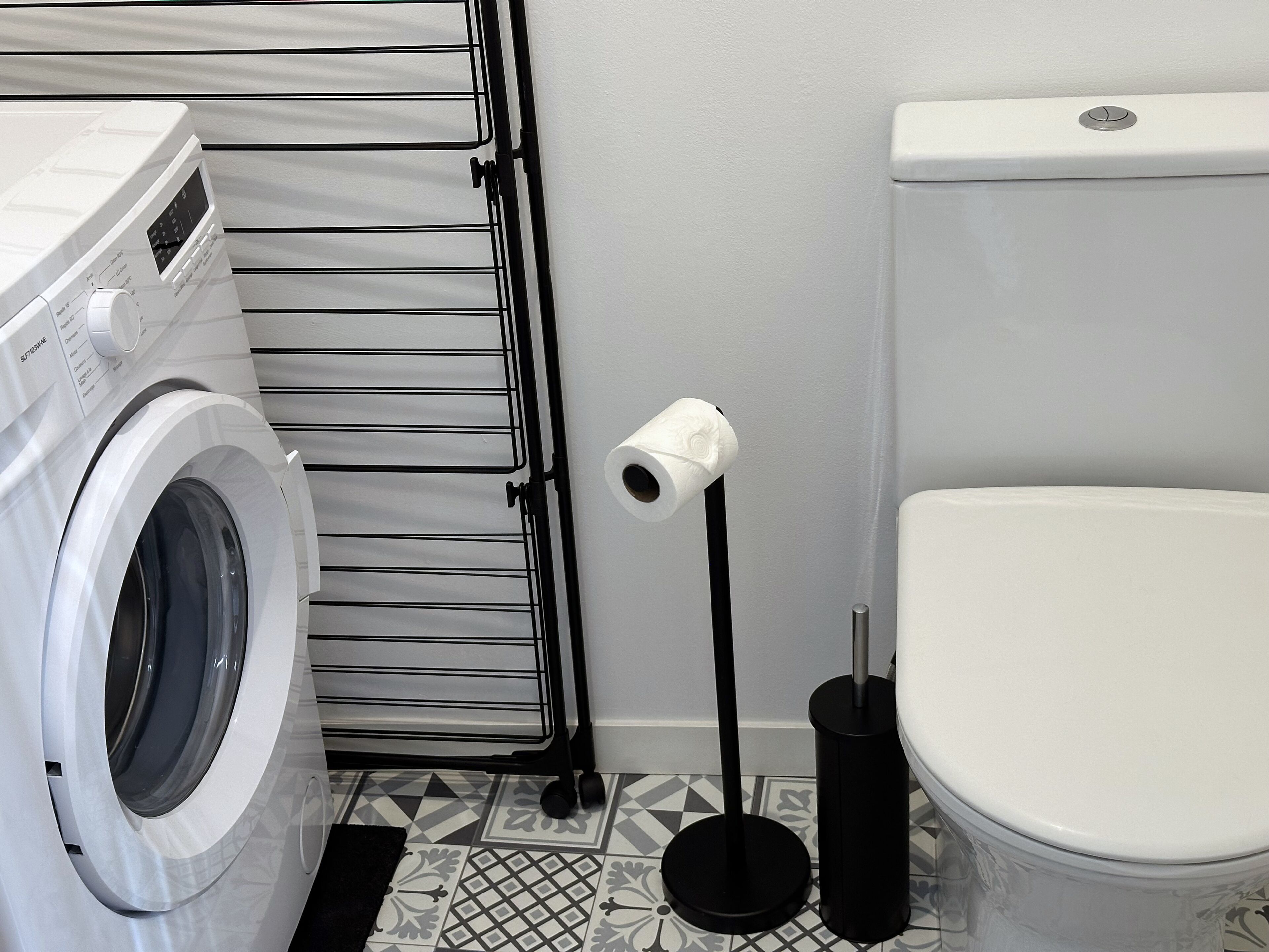 Et vaskerum med vaskemaskine, tørrestativ og toilet.