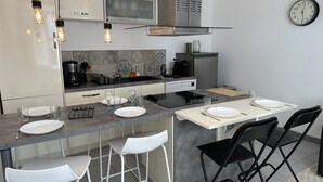 Une cuisine moderne avec un îlot central, des tabourets de bar, une table à manger et une horloge au mur.