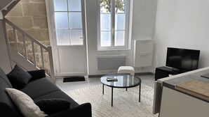 Un salon moderne comprenant un canapé, une petite table ronde, un téléviseur et un coin cuisine avec une planche à découper.