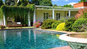 A pool with a bench and a building with columns and a covered porch. - Modern Studio set an Expansive Garden - 2253 (Harare)