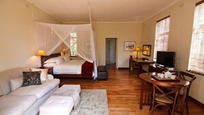 A hotel room with a bed, a sofa, a dining table with chairs, a TV, and a window with blinds. - Modern Studio set an Expansive Garden - 2253 (Harare)