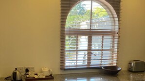 A kitchen with a window, a toaster, a kettle, and a bowl on the counter. - Modern Studio set an Expansive Garden - 2253 (Harare)