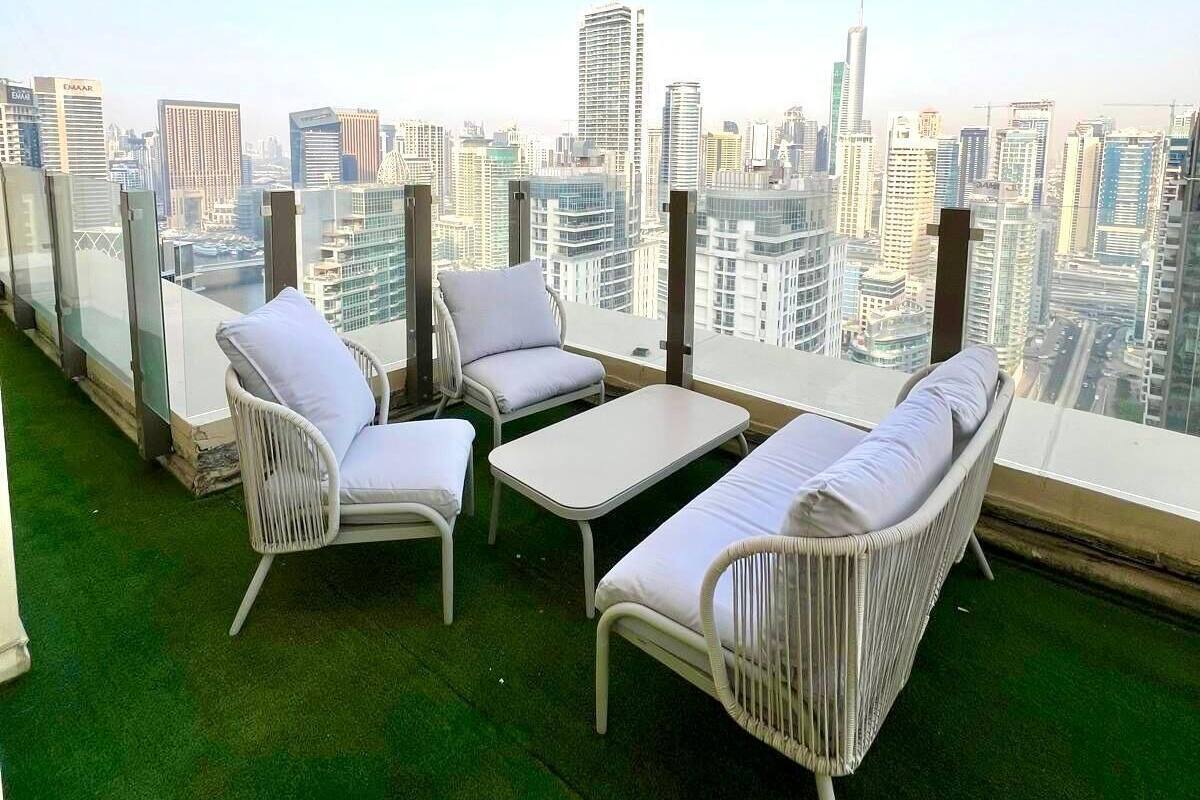 A rooftop terrace with white wicker furniture and a city view.