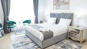 Une chambre à coucher moderne avec un grand lit, deux fauteuils, une table de chevet avec une lampe et un tableau au mur.