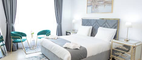 A modern bedroom with a large bed, two chairs, a bedside table with a lamp, and a painting on the wall.