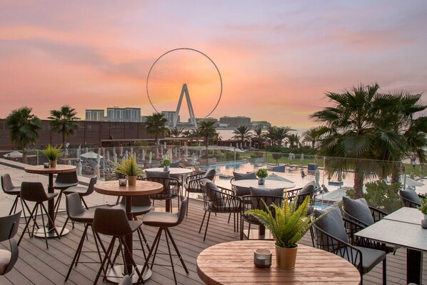 A rooftop bar with outdoor seating, a pool, and a Ferris wheel in the background.