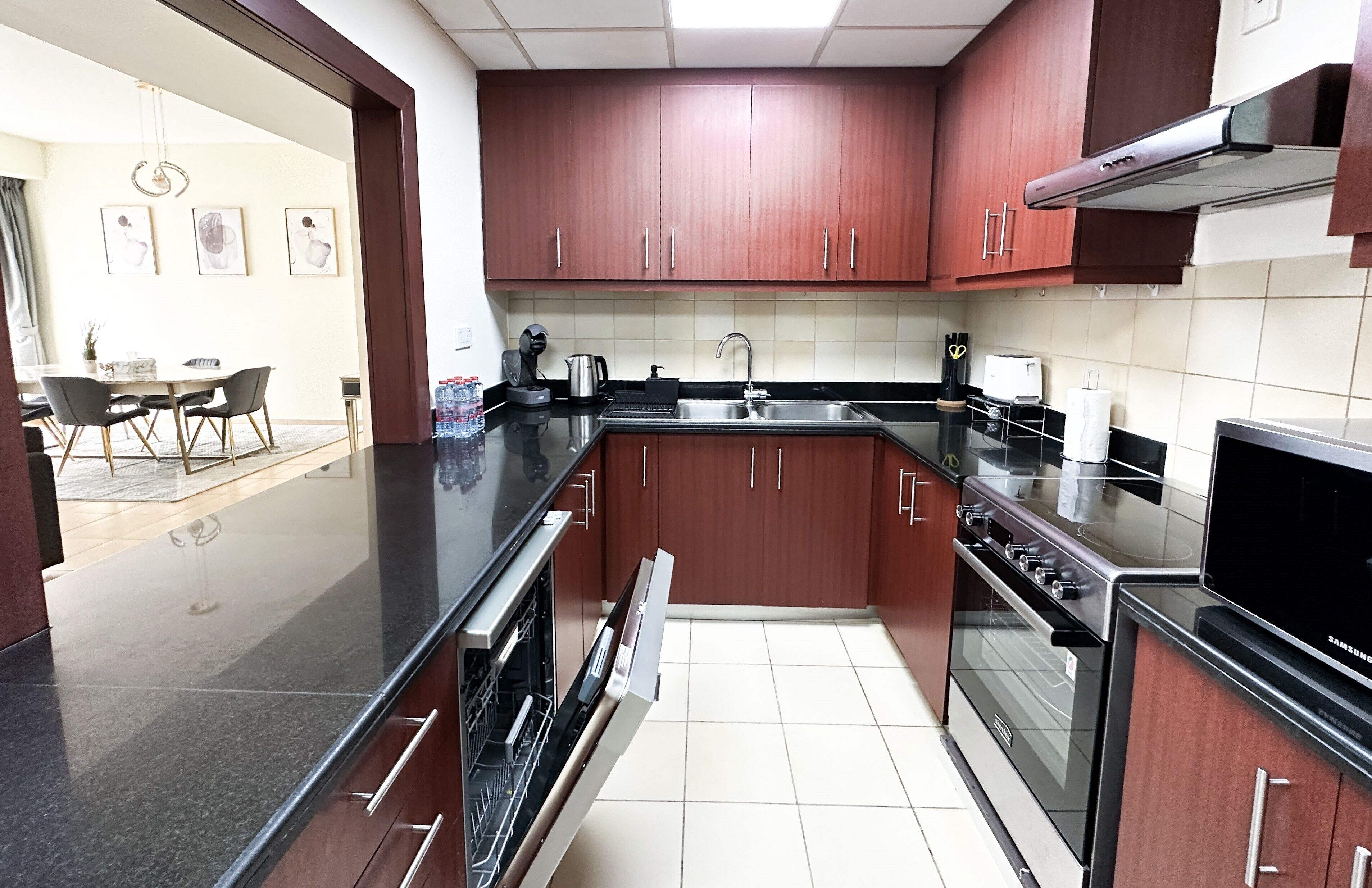 A modern kitchen with dark wooden cabinets, stainless steel appliances, and a black countertop.