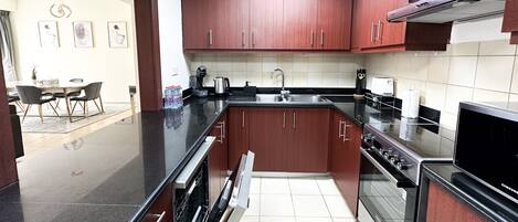 A modern kitchen with dark wooden cabinets, stainless steel appliances, and a black countertop.