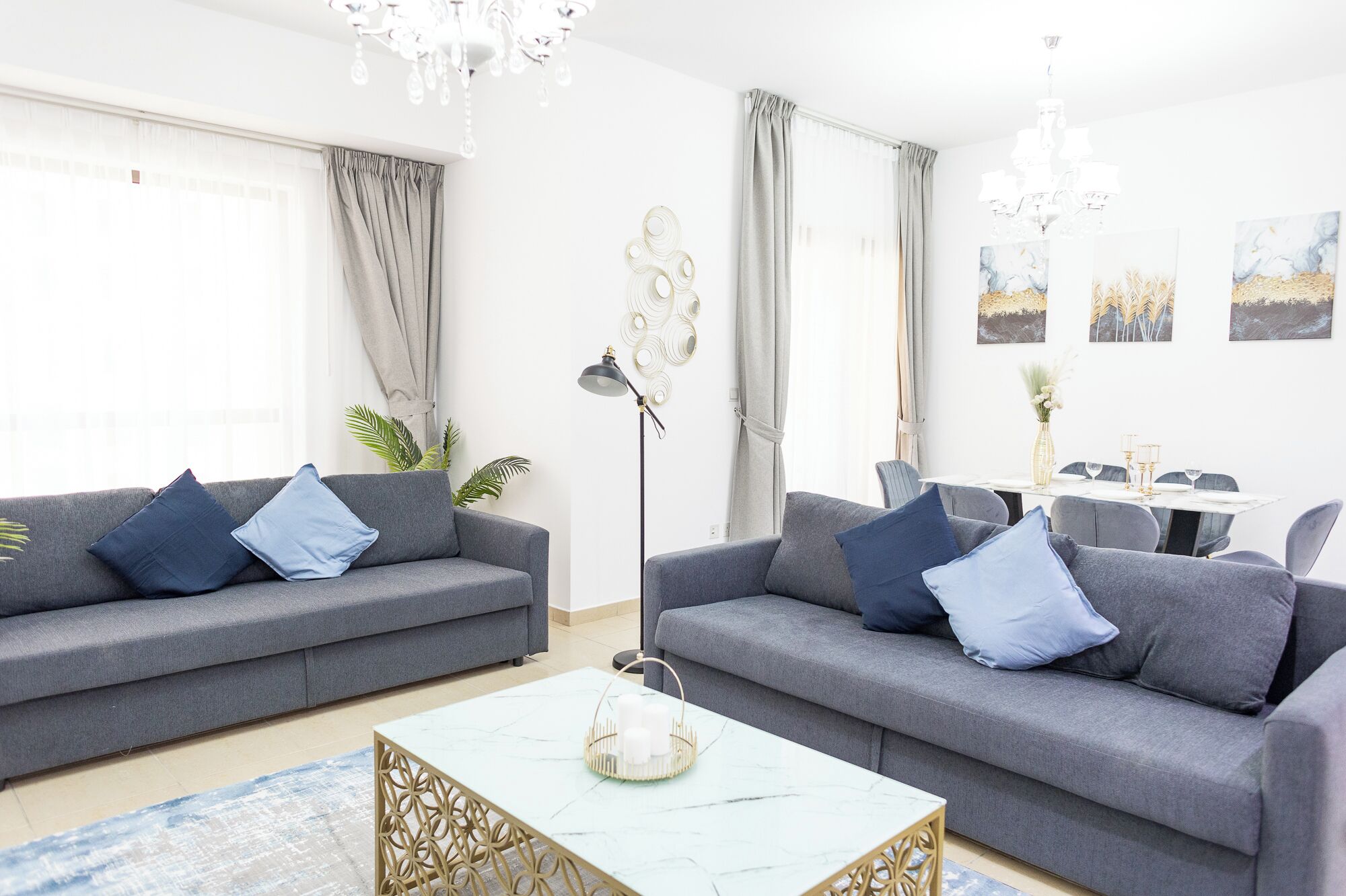 A modern living room with two grey sofas, a white coffee table, and a dining area with a table set for four.