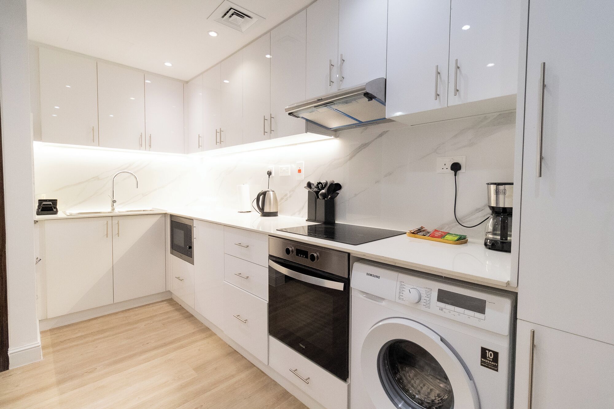 A compact kitchen with white cabinetry, a built-in oven, a microwave, a coffee maker, and a washing machine.
