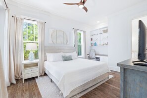 Quarto com cama, mesa de cabeceira, abajur e televisão sobre uma escrivaninha.