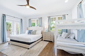 Une chambre à coucher avec un lit, une commode, un ventilateur de plafond et une fenêtre avec des rideaux.