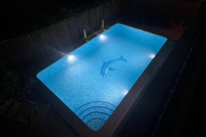 Una piscina rectangular con un adhesivo de delfín en el centro, rodeada por una valla de madera.